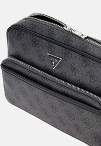 Borsa nera in finta pelle testurizzata con zip, dotata di due scomparti e un logo triangolare argentato sul davanti. Motivo goffrato sottile su tutto il tessuto.