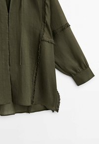 Oliven grøn, let bluse med en afslappet pasform, der har frynset kanter, knaplukning foran og blafrende ærmer.