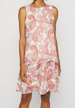 Robe blanche sans manches avec jupe superposée présentant des motifs cachemire roses, orange et beige, portée par une personne debout.