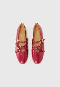 Ballerine in pelle rossa con più cinturini incrociati e fibbie in tonalità oro. Punta arrotondata e finitura testurizzata, con fodera interna beige.