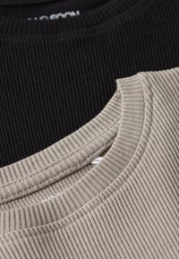 Gros plan sur les encolures en tissu côtelé de t-shirts à col rond beige et noir superposés.