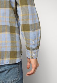 Camicia di flanella con un motivo a quadri blu, verde e giallo. Maniche lunghe con polsini abbottonati, realizzata in morbido tessuto intrecciato.