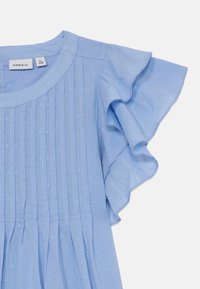 Robe bleu clair en tissu texturé, avec manches courtes à volants, plis verticaux et motifs décoratifs en points.