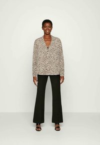 Blusa de manga longa com padrão de leopardo e decote em V, combinada com calças pretas de boca de sino. Textura suave, ajuste descontraído e detalhes mínimos.