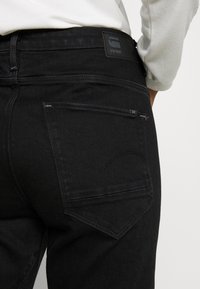 Černé džíny z denimu se zadní kapsou s jemným prošívaným vzorem a značkovou černou koženou nášivkou na pásku.