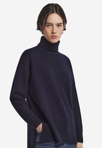 Marinblå polotröja med ribbad krage och fåll, som har en avslappnad passform och mjuk textur, gjord av ett varmt stickat material.