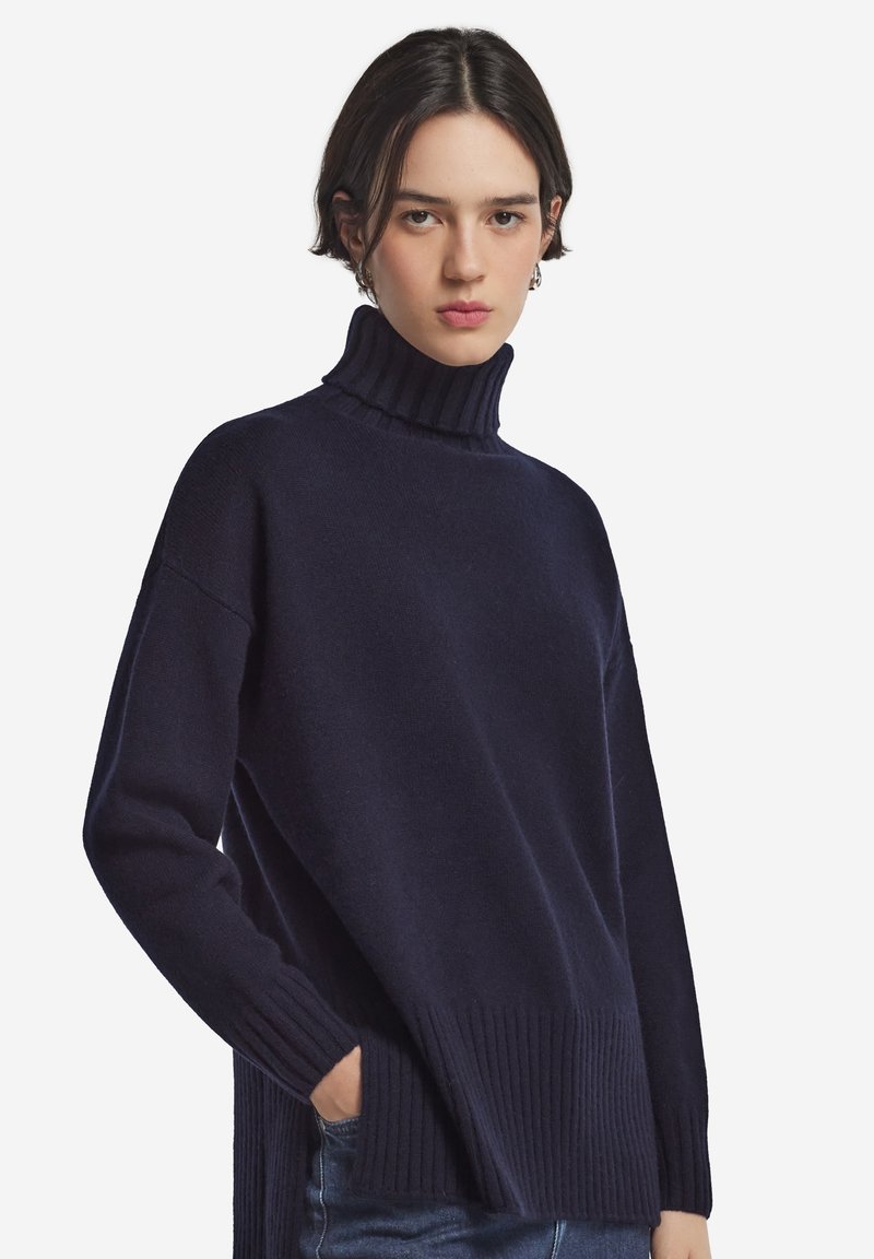 Marinblå polotröja med ribbad krage och fåll, som har en avslappnad passform och mjuk textur, gjord av ett varmt stickat material.