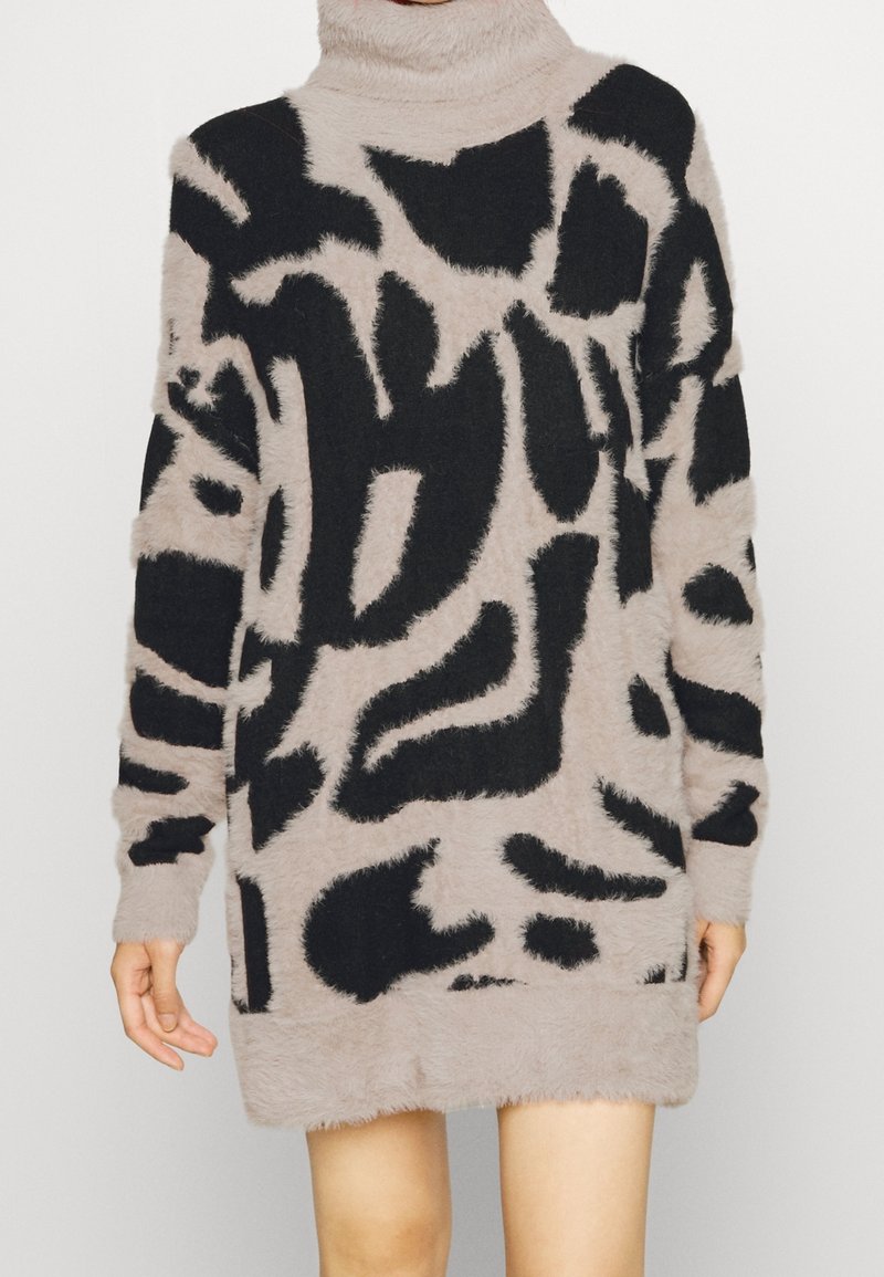 Maglione beige fuzzy a collo alto con motivi astratti neri, caratterizzato da maniche lunghe e una vestibilità morbida, che arriva a metà coscia. Tessuto soffice.