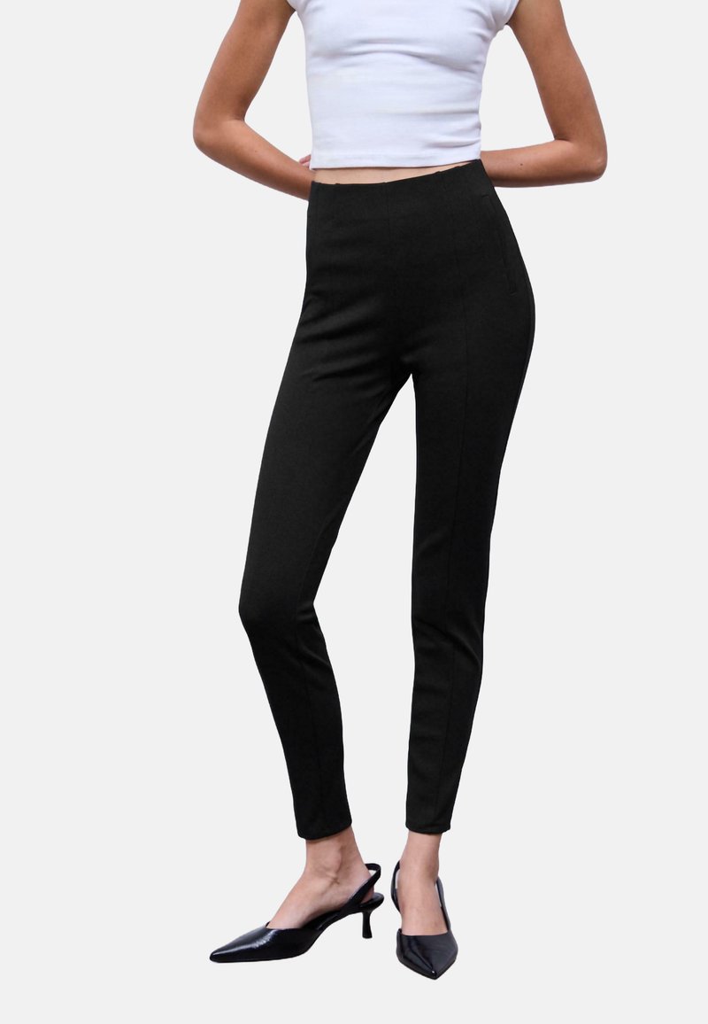 Pantaloni neri su misura con una vestibilità slim; presentano una vita alta e cuciture laterali. Abbinati a tacchi a punta neri, per un aspetto elegante.