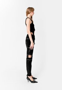 Top corto negro con detalle recortado combinado con pantalones negros que tienen costuras blancas en contraste y secciones recortadas en las rodillas. Tacones negros.