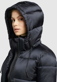 Giubbotto puffer navy con cappuccio, caratterizzato da un design trapuntato, chiusura con zip e cordini regolabili. Texture del tessuto liscia e lucida.