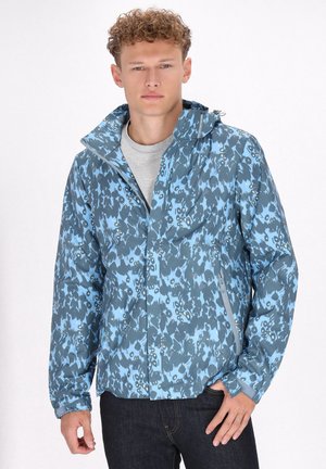 Giacca leggera blu con motivo camouflage; presenta un cappuccio, una zip frontale e polsini elasticizzati. Indossata su una maglietta grigia.