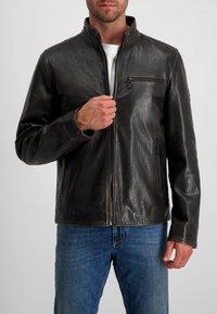 Schwarze Lederjacke mit hohem Kragen, Reißverschluss vorne und zwei Seitentaschen. Das Material hat eine strukturierte Oberfläche und sichtbare Nähte.