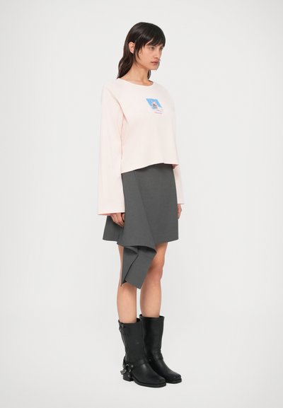 Hele roosa lühike pika varrukaga särk graafilise trükiga, sobitatud halli asümmeetrilise mähkkleitiga ja mustade põlveni ulatuvate saapadega.