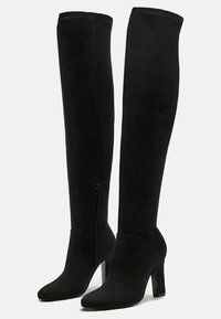Bottes noires au-dessus du genou en daim doux avec une texture lisse, dotées d'un talon aiguille et d'une fermeture éclair sur le côté pour un enfilage facile.