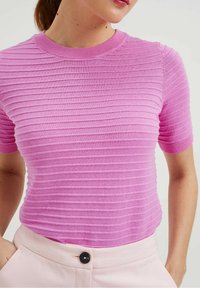 Tajta rosa ribbad tröja med rund halsringning och korta ärmar. Texturen har horisontella ränder, i kombination med ljusa byxor.