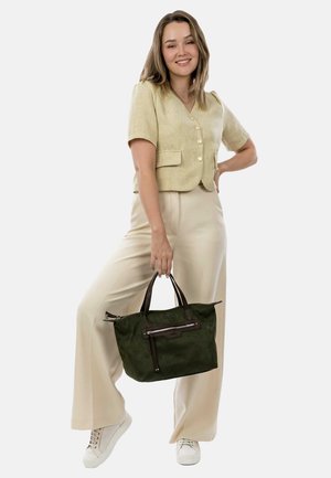Sac en daim vert avec des accents en cuir, porté par une personne vêtue d'une veste courte à manches courtes en tissu léger et de pantalons larges beige.