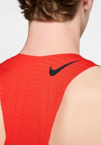 Punane sportlik tank top, millel on perforeritud kangas, ümar kaelus ja must Nike logo, mis asub ülemises seljas.