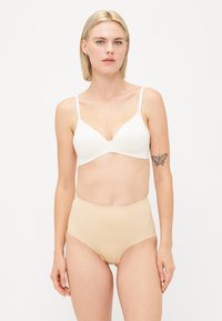 Witte draadloze beha met een V-hals ontwerp, gladde cups en verstelbare bandjes, gecombineerd met naadloze, huidskleurige hooggekapte onderbroek.