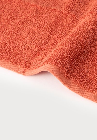 Gros plan sur une serviette orange corail pliée, mettant en valeur sa texture douce en éponge bouclée et son bord ourlé sur fond blanc.