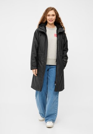 Manteau long noir imperméable avec capuche, doté d'une taille cintrée, de boutons-pression et de poches latérales, porté sur un sweat gris et un jean bleu.