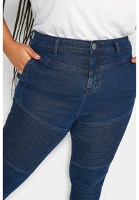 Vaqueros de mezclilla azul con un diseño ajustado. Presenta una textura acanalada en la parte inferior de las piernas, cinco bolsillos y una cintura alta con un cierre de botón en la parte frontal.