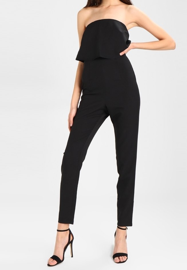 Czarny bezramienny kombinezon z rozkloszowanym topem, zwężającymi się nogawkami i długością do kostek. Połączony z czarnymi szpilkami. Gładka faktura materiału.