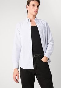 Camisa de botones en rayas azul claro y blanca, hecha de algodón, con cuello clásico y mangas largas, combinada con jeans ajustados negros.