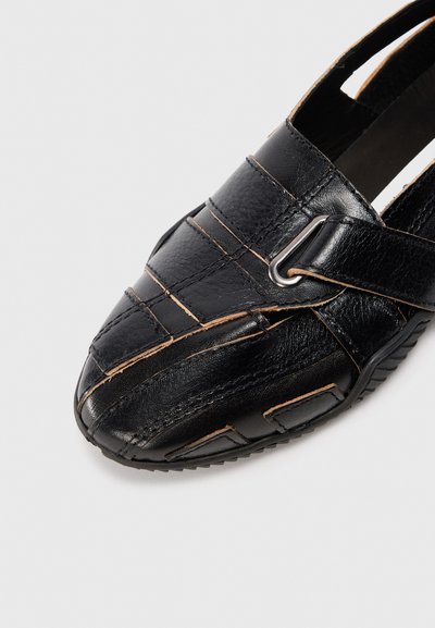 Svart lädersko med korslagd design, texturerad yta, silverfärgad detalj och gummisula med spetsig tå.