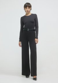 Top nero a maniche lunghe abbinato a pantaloni neri a vita alta e larghi fissati con una cintura nera lucida e tacchi neri a punta.