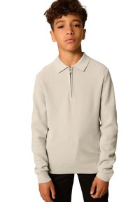 Light gray pullover with a zip collar, ribbed texture, long sleeves, and fitted cuffs. Worn over black pants. Simple and functional design.