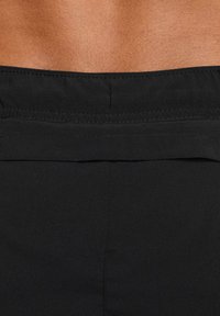 Bañador negro con una textura suave, que presenta una cinturilla horizontal y costuras limpias, mostrando parte de una espalda bronceada por encima de la cintura.