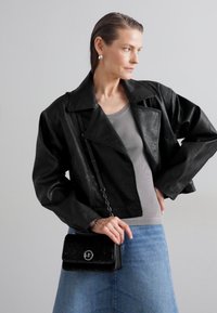 Veste courte en cuir noir avec des revers larges, associée à un haut gris côtelé et à une jupe en denim bleu. Tenant un petit sac noir avec un logo.