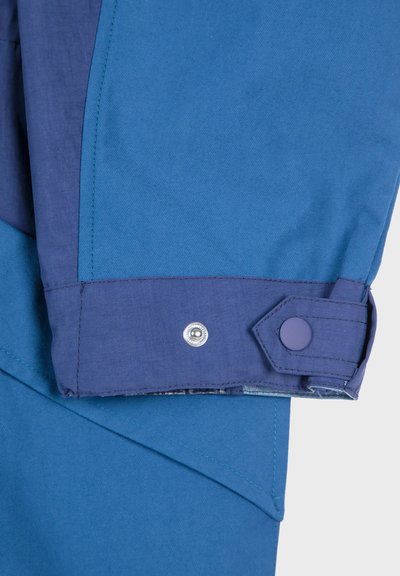 Blue waterproof jacket featuring a purple cuff with a snap button and contrasting stitching; smooth texture with angular design details.