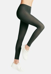 Leggings verdi scuri a vita alta realizzati in materiale liscio ed elasticizzato; design aderente con stile alla caviglia; abbinati a sneaker bianche.