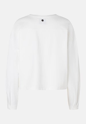 Weißes, kurz geschnittenes Sweatshirt mit langen Ärmeln, überschnittenen Schultern und kleinem schwarzem Logo-Patch nahe dem Rückenausschnitt.