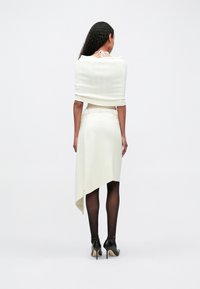 Λευκ�ό, ριμπ πλεκτό τοπ ελαφριάς υφής με κομψό κοντό μήκος, συνοδευόμενο από ασύμμετρη φούστα με μήκος μέχρι το γόνατο. Μαύρες ψηλοτάκουνες γόβες και διάφανα καλσόν.