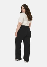 Kurig geschnittenes, hellcremiges Oberteil mit kurzen Ärmeln. Schwarze, weite Hose mit einem elastischen Bund. Legere weiße Sneakers.