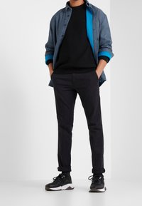 Black sweater layered under a blue and checkered button-up shirt, paired with dark pants and black sneakers with white accents.