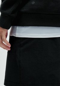 Zwarte sweatshirt over een wit sportshirt, gecombineerd met een zwarte rok met een zijzak en zichtbare stiksels.