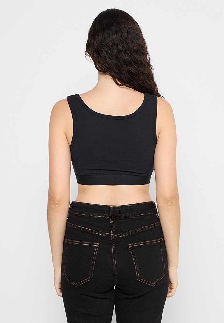 Crop top noir en coton avec un col rond, des bretelles fines et une texture lisse, associé à un jean noir taille haute avec des coutures orange.