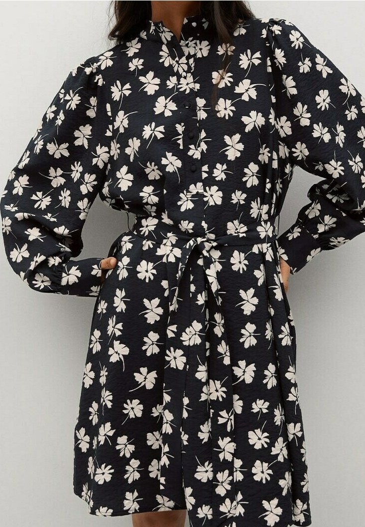 Robe noire à motif floral blanc, manches longues bouffantes, devant boutonné et ceinture nouée à la taille.
