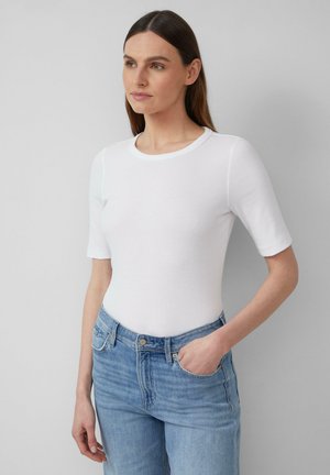 Haut blanc à manches courtes avec un col rond, associé à un jean en denim bleu clair. Le tissu semble doux et ajusté.