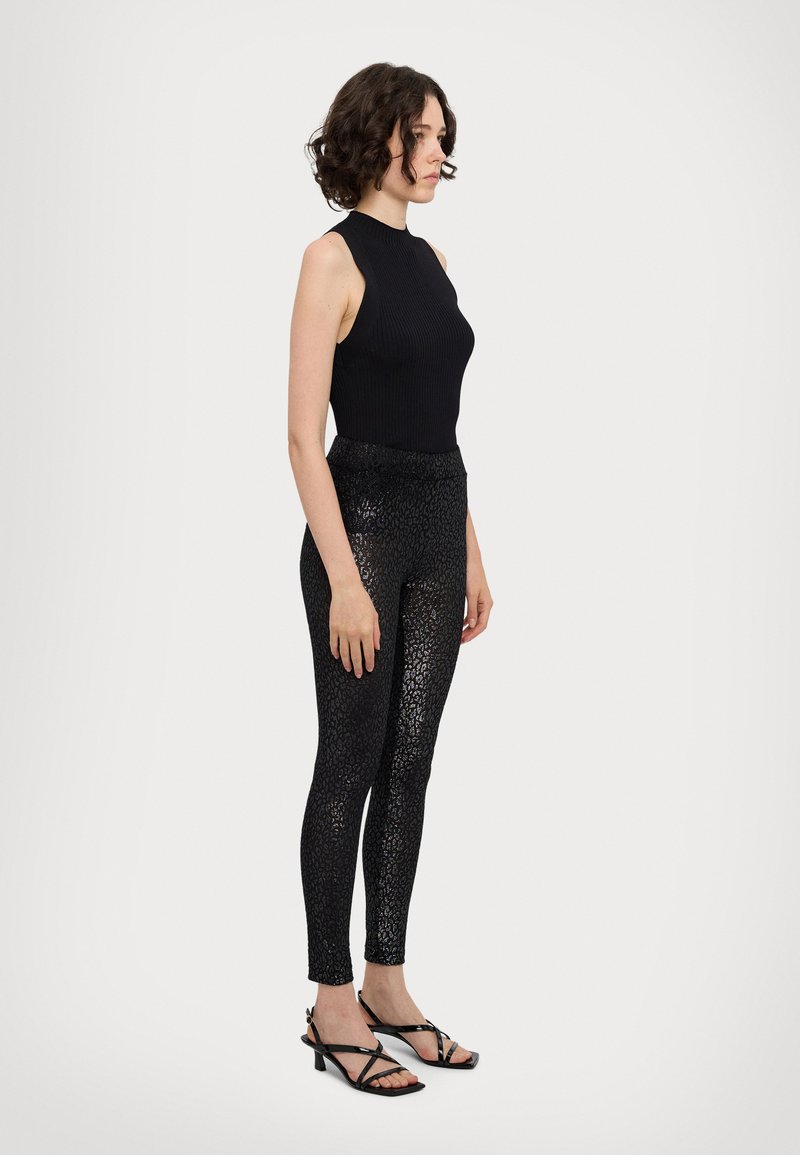 Čierny rebrovaný top bez rukávov v kombinácii s čiernymi legínami so lesklým vzorom leopardích škvŕn a čiernymi sandálmi na podpätku.