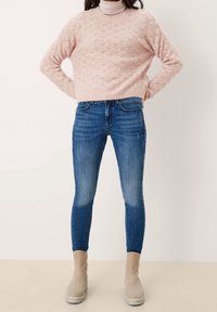 Pull en tricot rose clair avec un motif en losange, associé à un jean skinny bleu foncé et des bottines beiges à semelle plateforme.