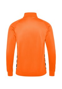 Orange lynlås sportsjakke med høj krave, lange ærmer og sidelister med et kontrastfarvet sort og hvidt geometrisk mønster.