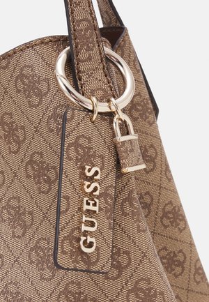 Gros plan d’un sac à main marron Guess avec motif monogramme texturé, anneau en métal doré et une étiquette indiquant le nom de la marque GUESS en lettres dorées.