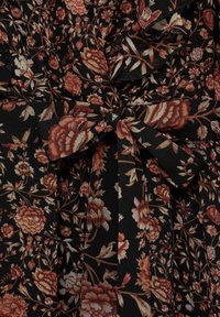 Tissu noir avec des motifs floraux complexes dans des nuances d'orange et de crème. Présente un lien en tissu à la taille et des volants superposés.