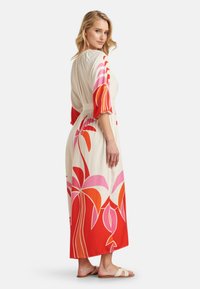 Maxi dress in cream, featuring large red, pink, and orange floral print. Short puff sleeves and a cinched waist, paired with light sandals.