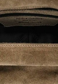 Intérieur d'un sac à main en cuir suédé marron montrant une étiquette cousue avec le nom de la marque et une petite poche zippée.